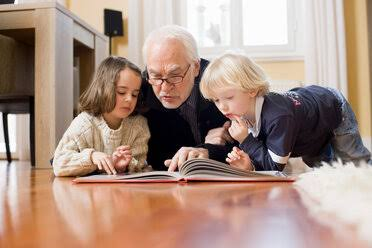 Grandfather reading with two grandchildren at home